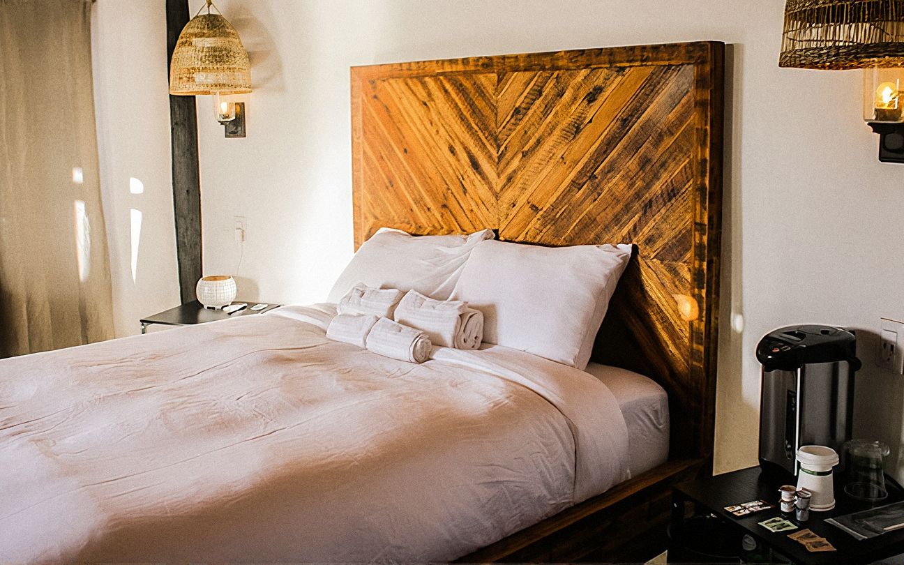Interior del Bungalow de Tierra 01 con cama, cabecera de madera en espiga y lámparas colgantes de ratán