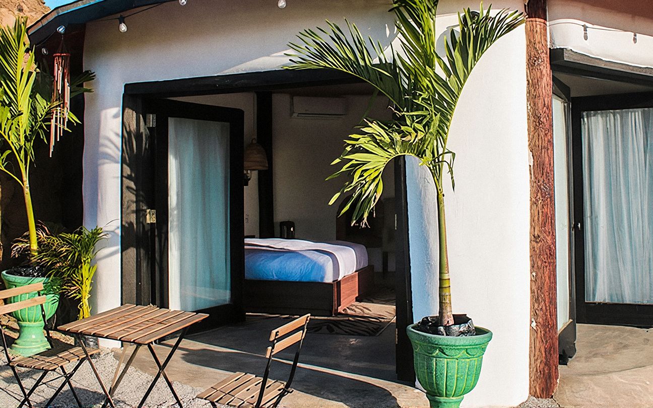 Exterior del Bungalow de Tierra 03, redondo y blanco, con palmeras en macetas y mesa en la terraza