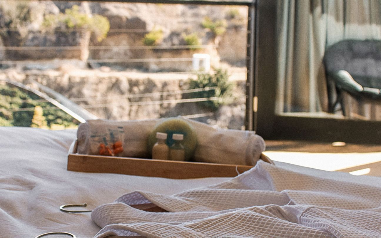 Cama de la Cabaña de Madera 02 con charola de bienvenida y bata doblada frente al ventanal con vista a la ladera