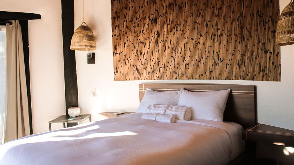 Cama con almohadas blancas y toallas enrolladas en la recámara de un bungalow de Raíz Resort