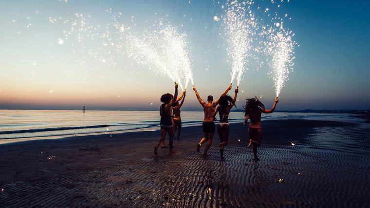 Grupo de amigos con bengalas encendidas corriendo por la playa al anochecer