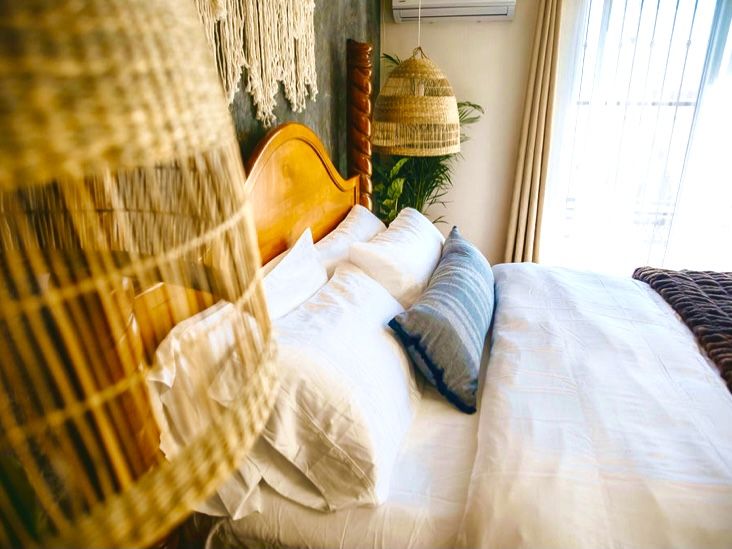 Detalle de la cama con sábanas blancas, almohadas de plumas y lámpara de ratán
