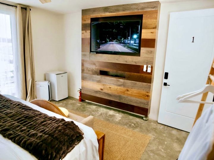 Vista de la Habitación 01 hacia la pantalla de TV en muro de madera y la puerta con cerradura de código