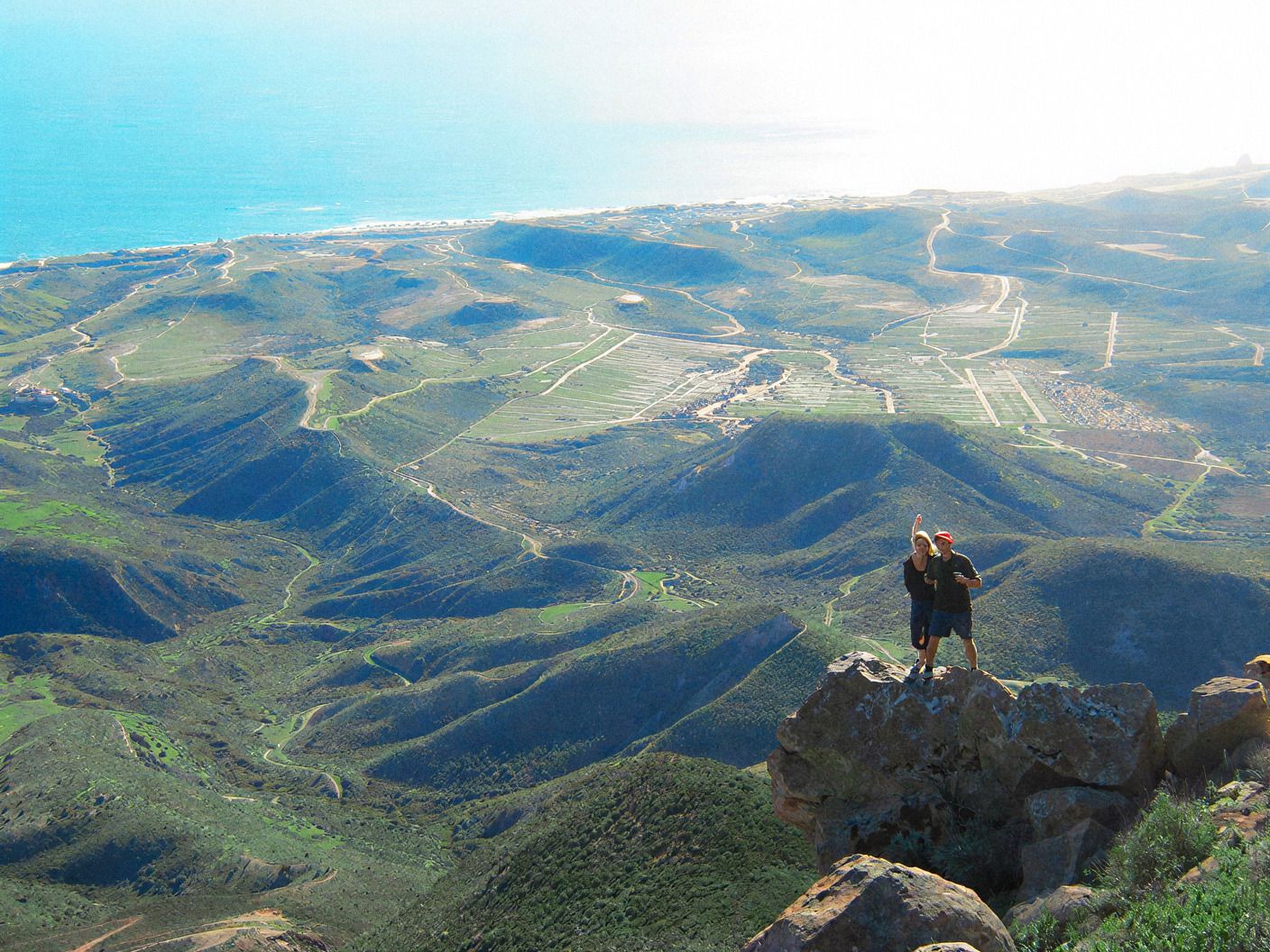 Excursionista en la cima del Cerro El Coronel con vista a las colinas verdes y la costa de Rosarito