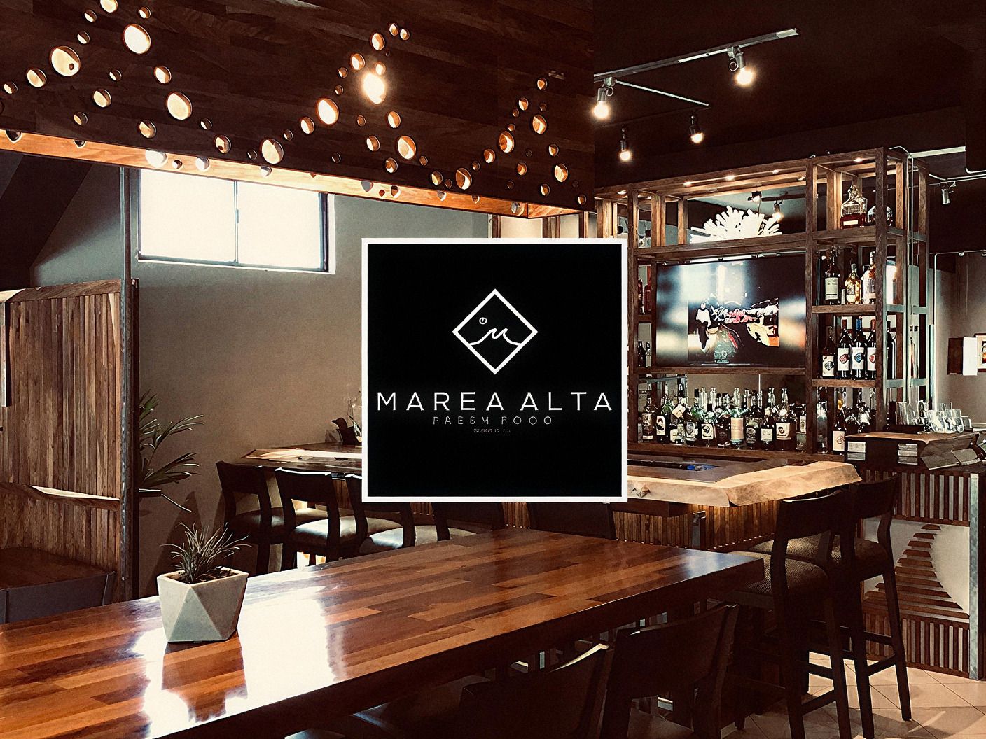Interior de madera con barra y luces colgantes del restaurante de mariscos Marea Alta en Rosarito