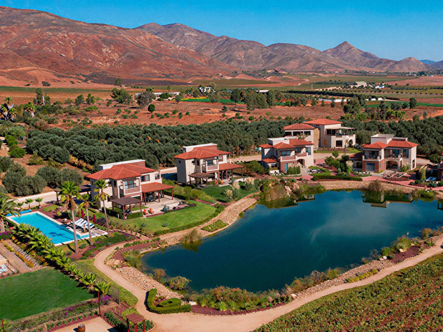 Vista aérea del Valle de Guadalupe con viñedos, casas, alberca y una presa entre montañas